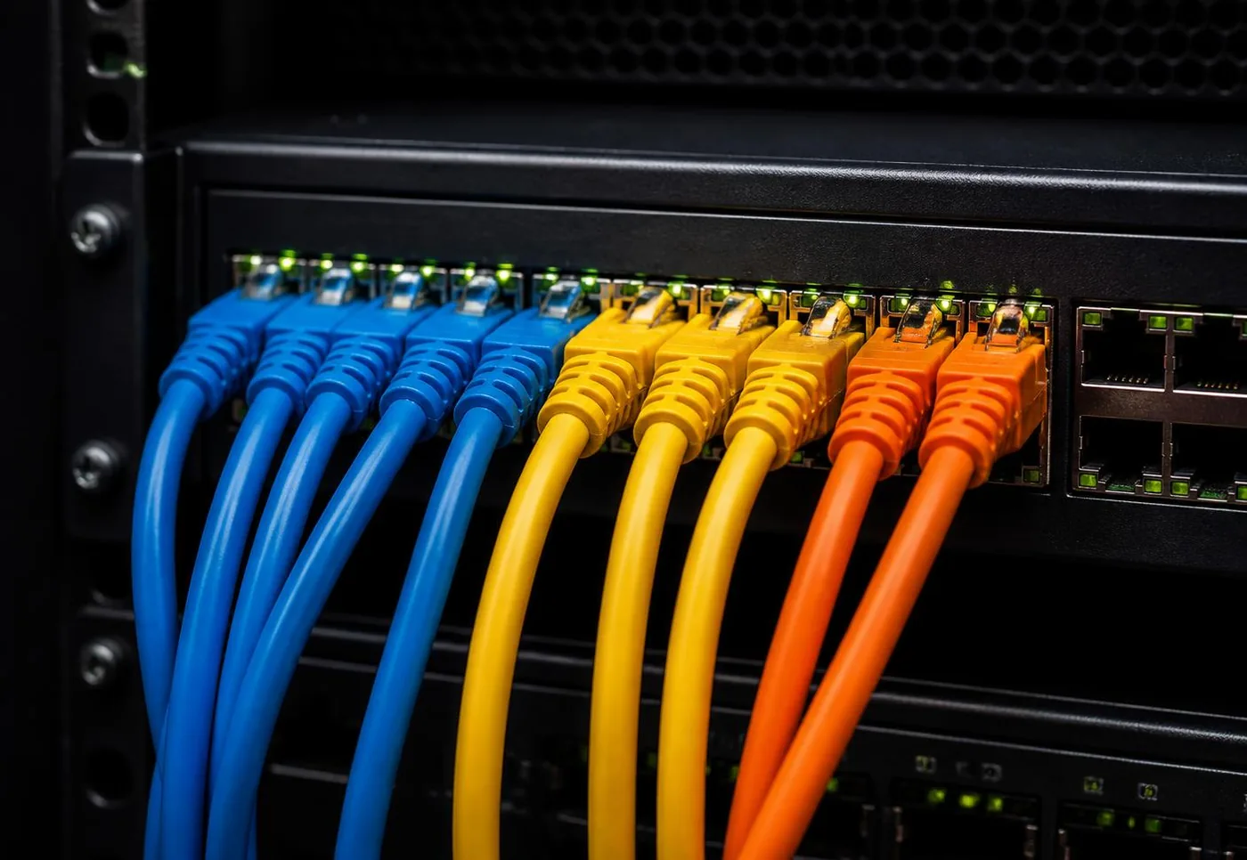 Câbles réseau bleus, jaunes et orange raccordés à un switch professionnel avec voyants LED