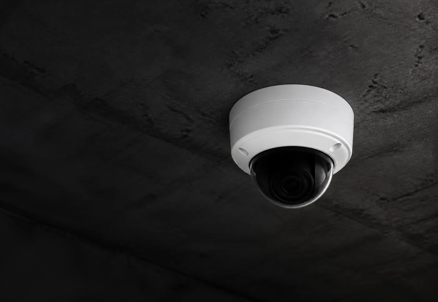 Caméra de surveillance dôme blanche fixée à un plafond sombre, vue en contre-plongée